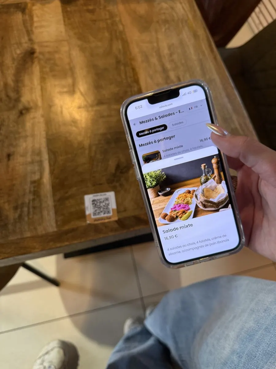 La fiche de la Salade mixte à 16,90 € s’ouvre sur un téléphone, avec sa photo améliorée par notre Studio Photo intégré, au-dessus de l’Autocollant QR.