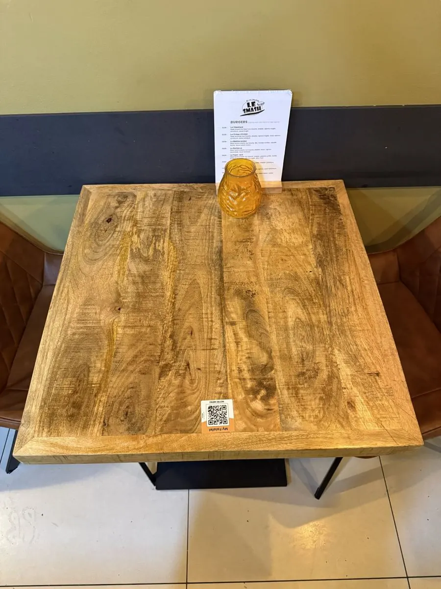 Sur une table de My Falafel, la carte papier des smash burgers tient sur un chevalet en bois, et l’Autocollant QR est collé au bord de la table.